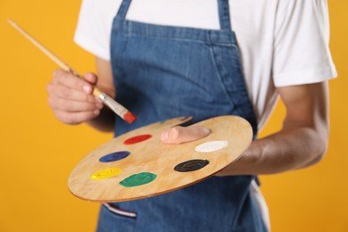 Photo of Man with palette and paintbrush on orange background, closeup