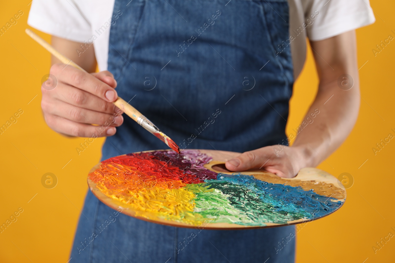 Photo of Man with palette and paintbrush on orange background, closeup