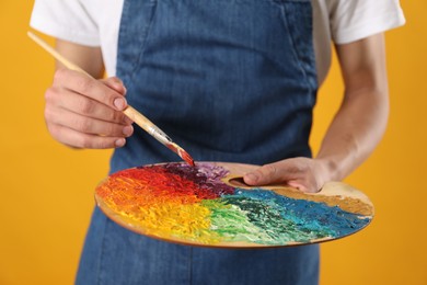 Photo of Man with palette and paintbrush on orange background, closeup