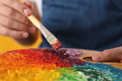 Man with palette and paintbrush on orange background, closeup