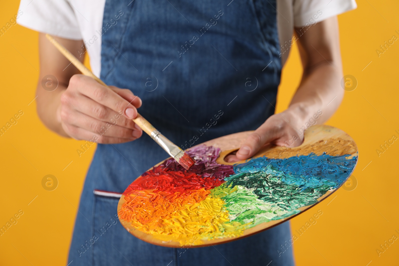 Photo of Man with palette and paintbrush on orange background, closeup