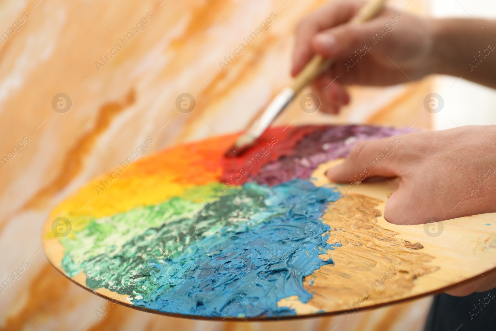 Photo of Man with paintbrush mixing paints on palette, closeup