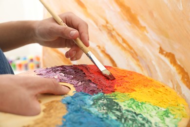 Photo of Man with paintbrush mixing paints on palette, closeup