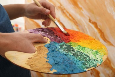 Photo of Man with paintbrush mixing paints on palette, closeup