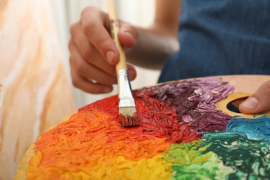 Photo of Man with paintbrush mixing paints on palette, closeup