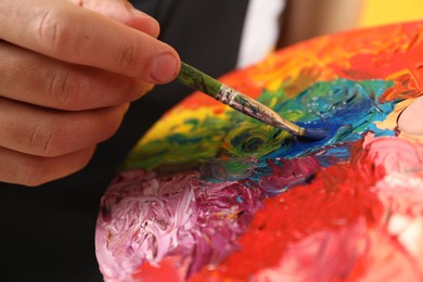 Photo of Man with paintbrush mixing paints on palette, closeup