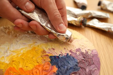 Man squeezing paint from tube onto palette at wooden table, closeup