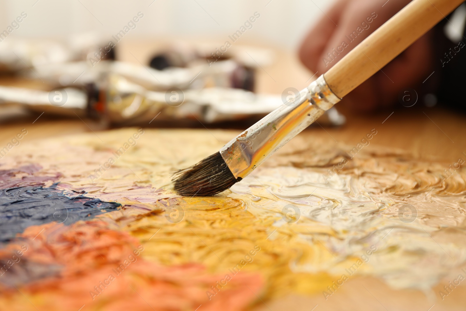 Photo of Mixing paints on palette with brush at table, closeup