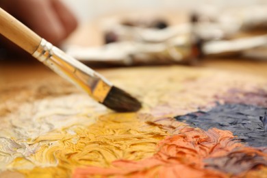 Photo of Mixing paints on palette with brush at table, closeup