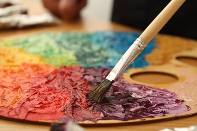 Photo of Mixing paints on palette with brush at table, closeup