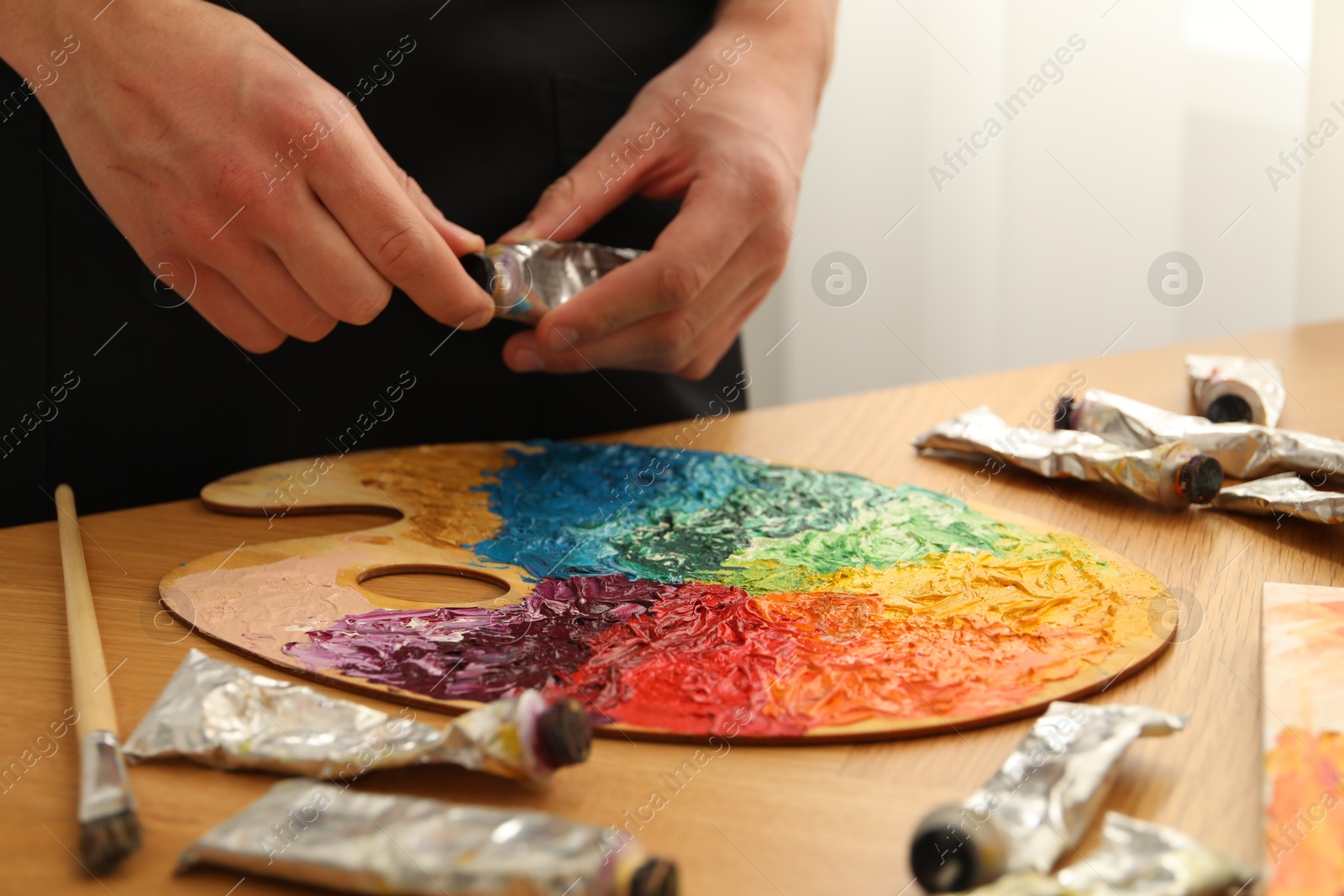 Photo of Man opening tube of paint at table with palette indoors, closeup