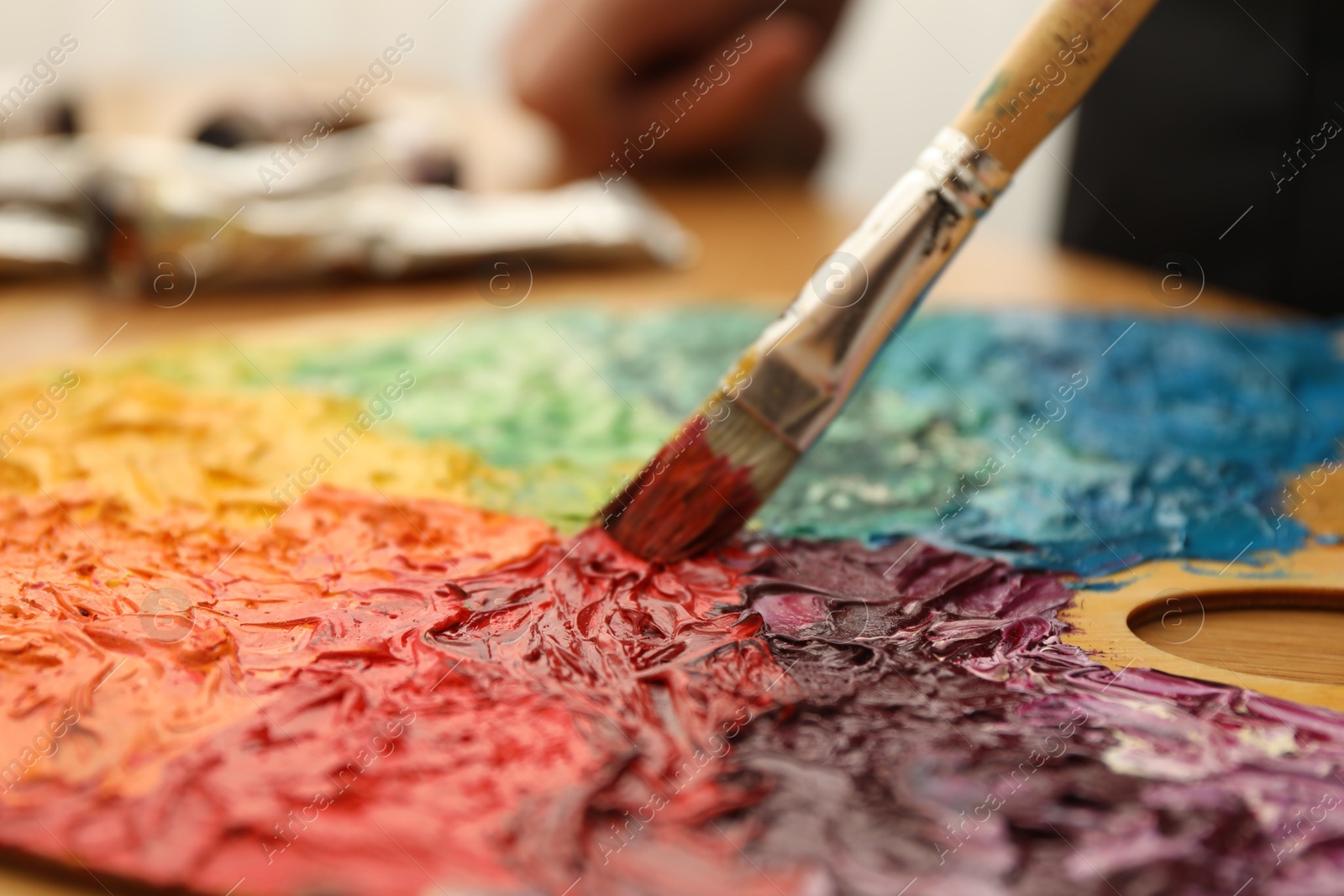 Photo of Mixing paints on palette with brush at table, closeup