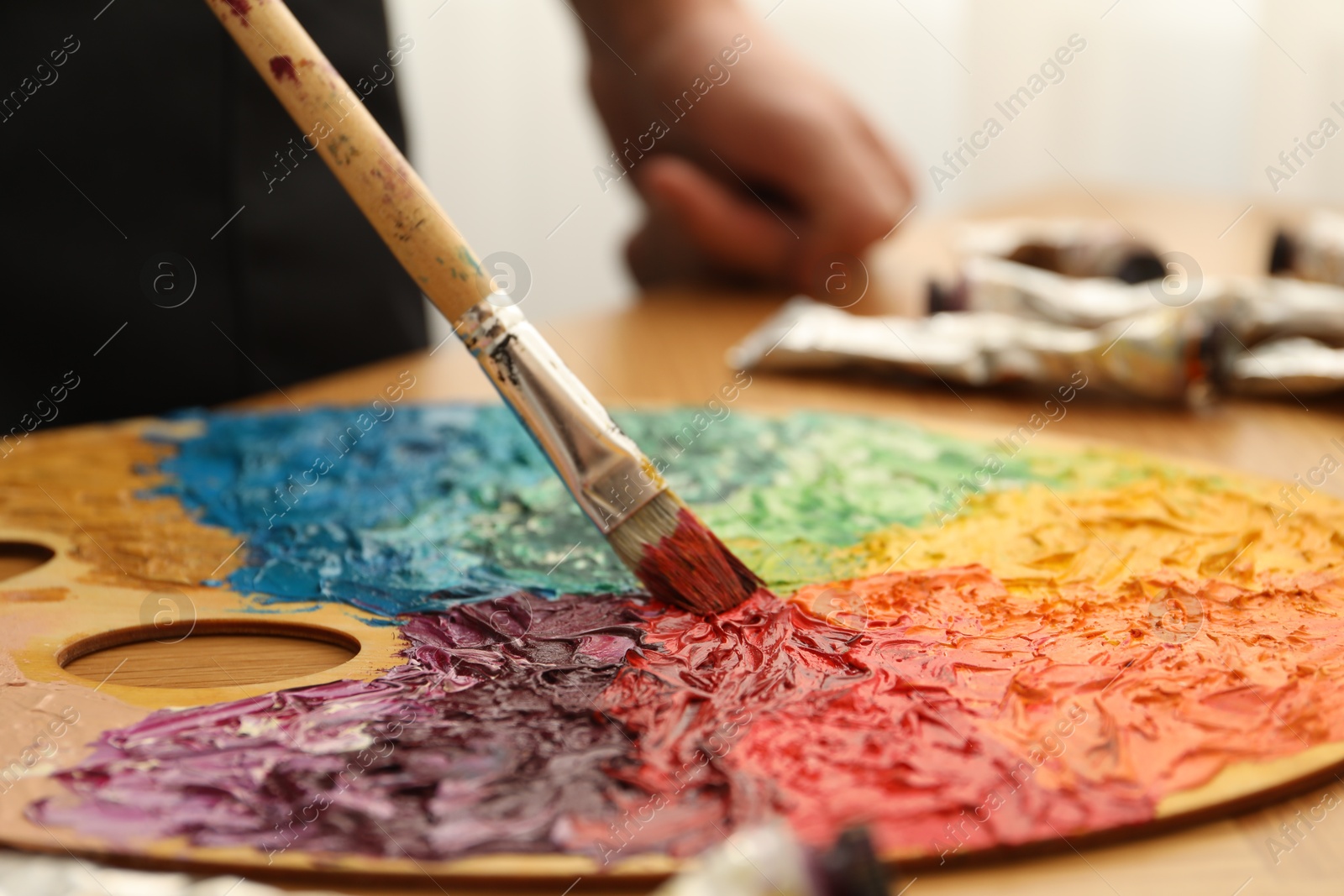 Photo of Mixing paints on palette with brush at table, closeup