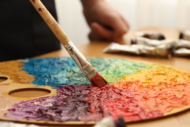 Photo of Mixing paints on palette with brush at table, closeup