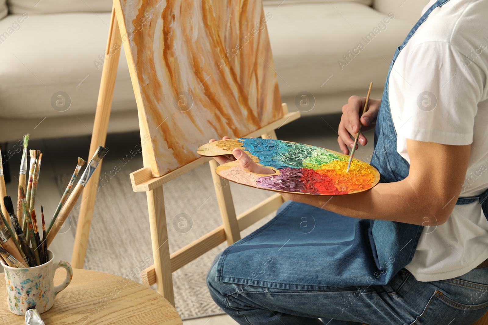 Photo of Man with palette and paintbrush drawing picture indoors, closeup