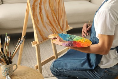 Photo of Man with palette and paintbrush drawing picture indoors, closeup