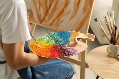 Photo of Man with palette and paintbrush drawing picture indoors, closeup