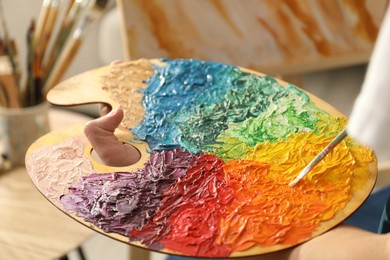 Man with paintbrush mixing paints on palette indoors, closeup