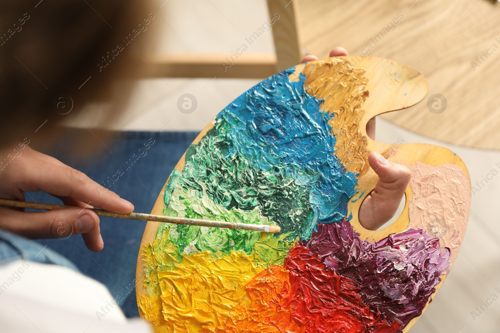 Photo of Man with paintbrush mixing paints on palette indoors, closeup