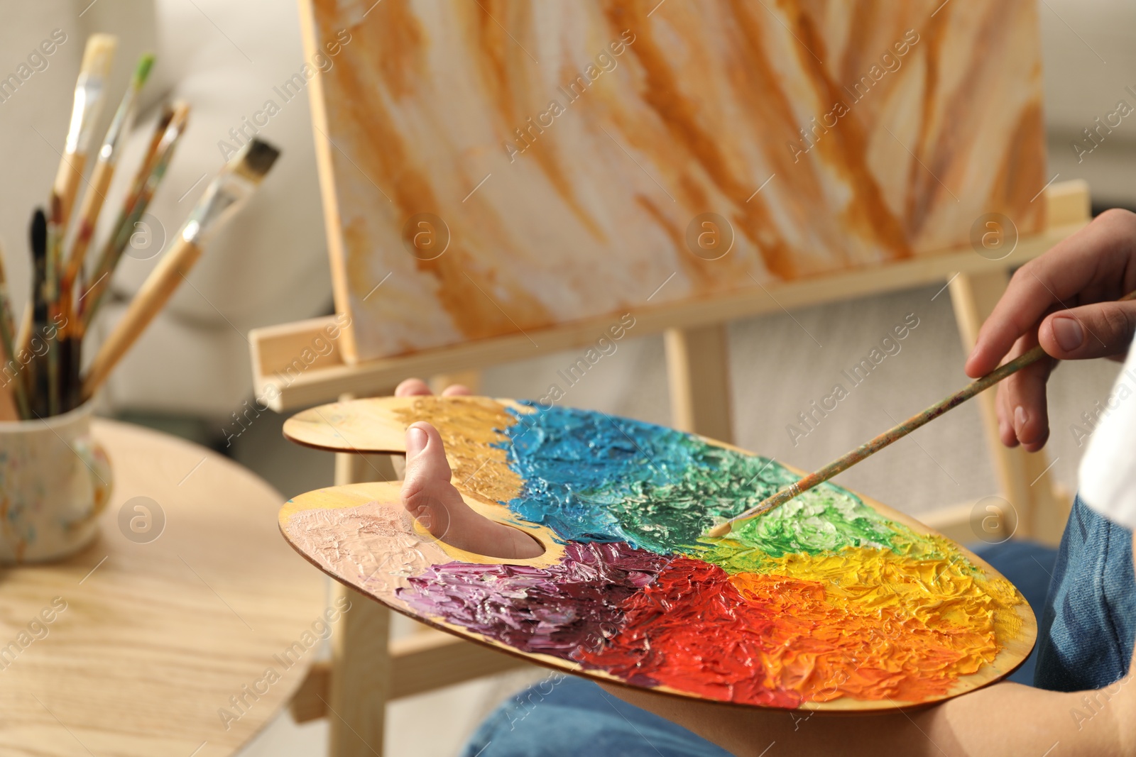 Photo of Man with paintbrush mixing paints on palette indoors, closeup