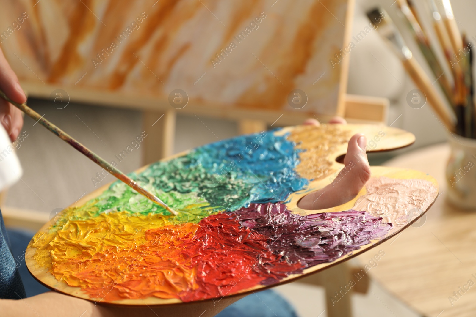 Photo of Man with paintbrush mixing paints on palette indoors, closeup