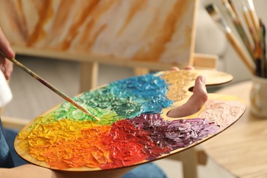 Photo of Man with paintbrush mixing paints on palette indoors, closeup