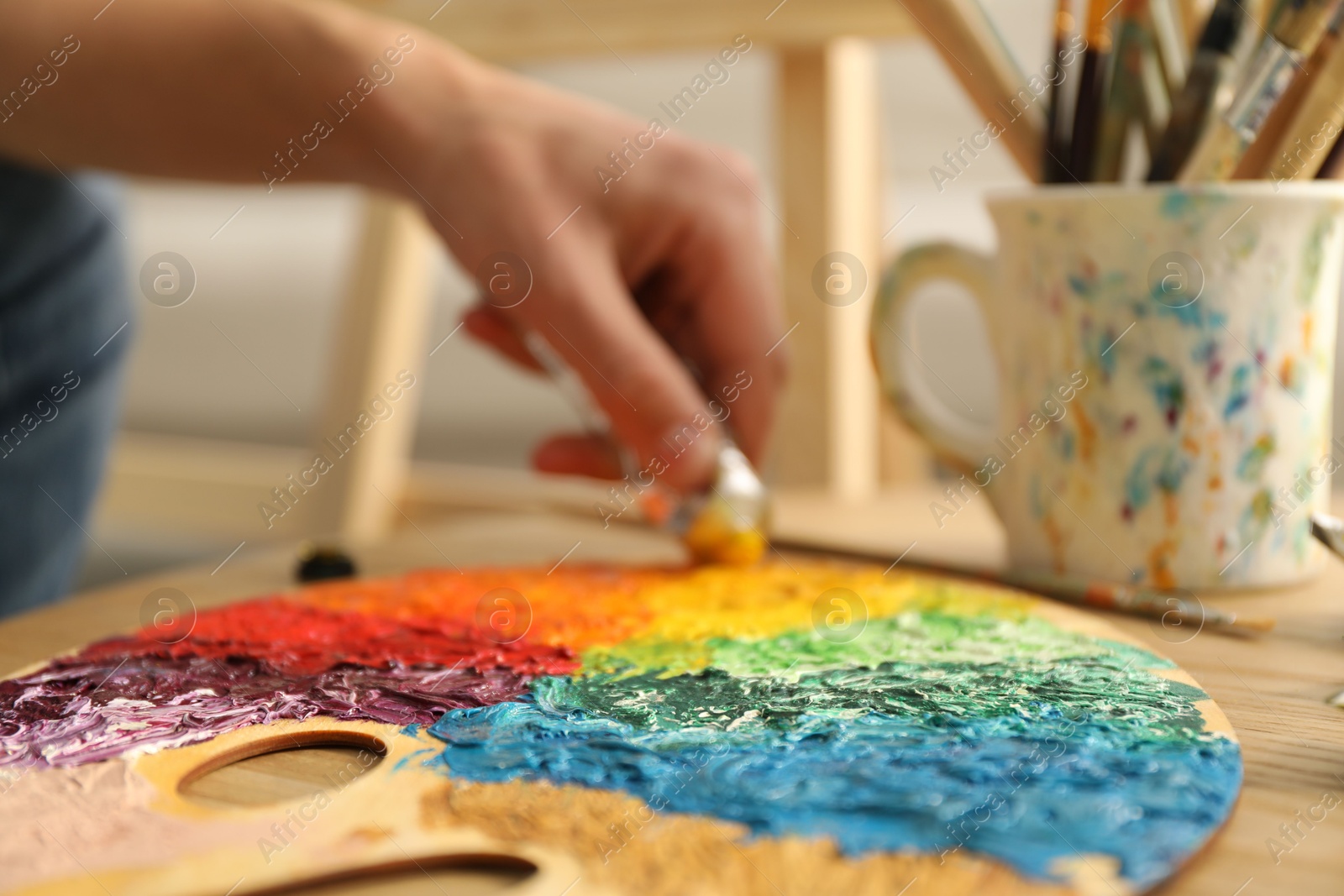 Photo of Man squeezing paint from tube onto palette at wooden table indoors, selective focus