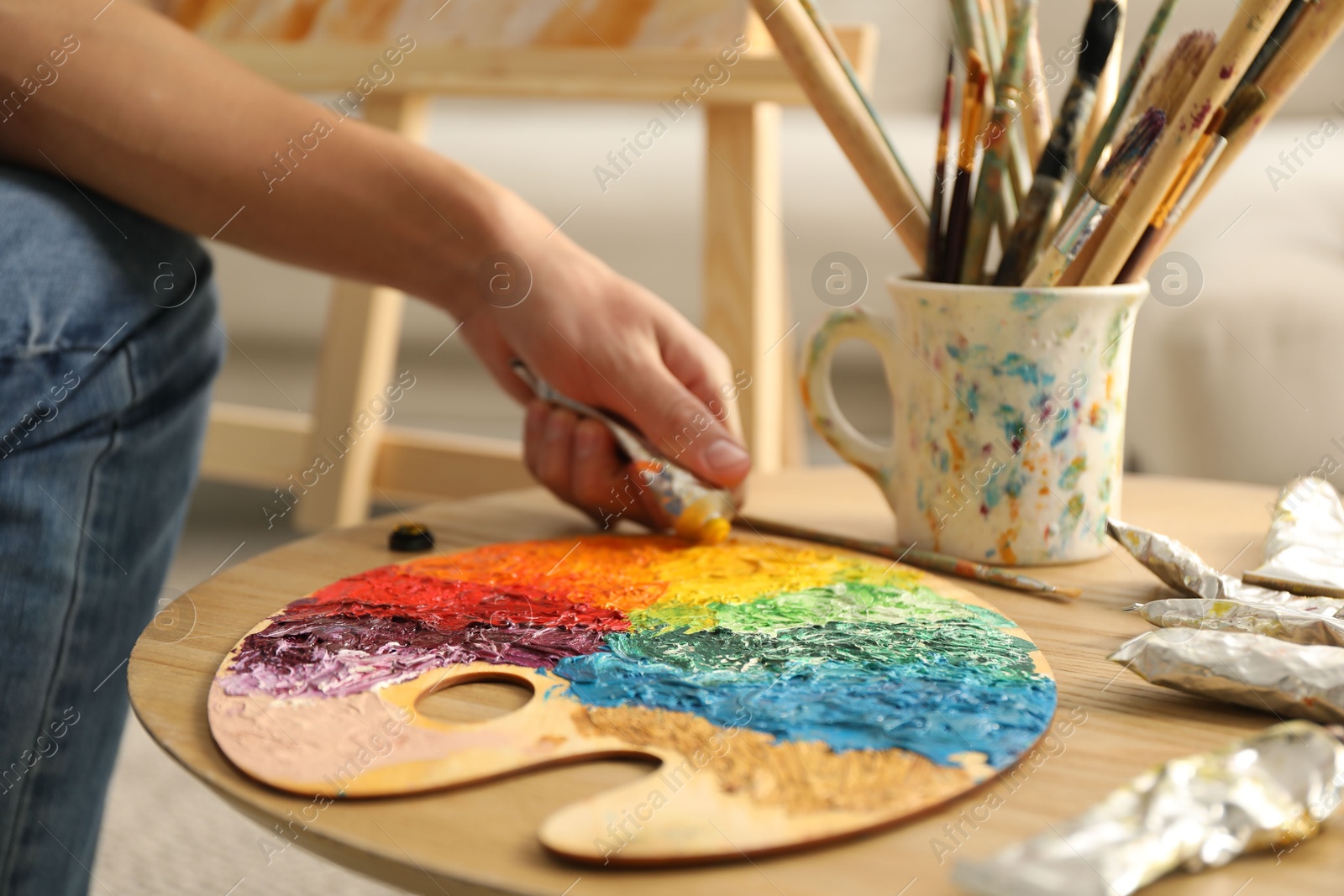 Photo of Man squeezing paint from tube onto palette at wooden table indoors, closeup