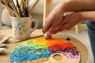 Photo of Man squeezing paint from tube onto palette at wooden table indoors, closeup