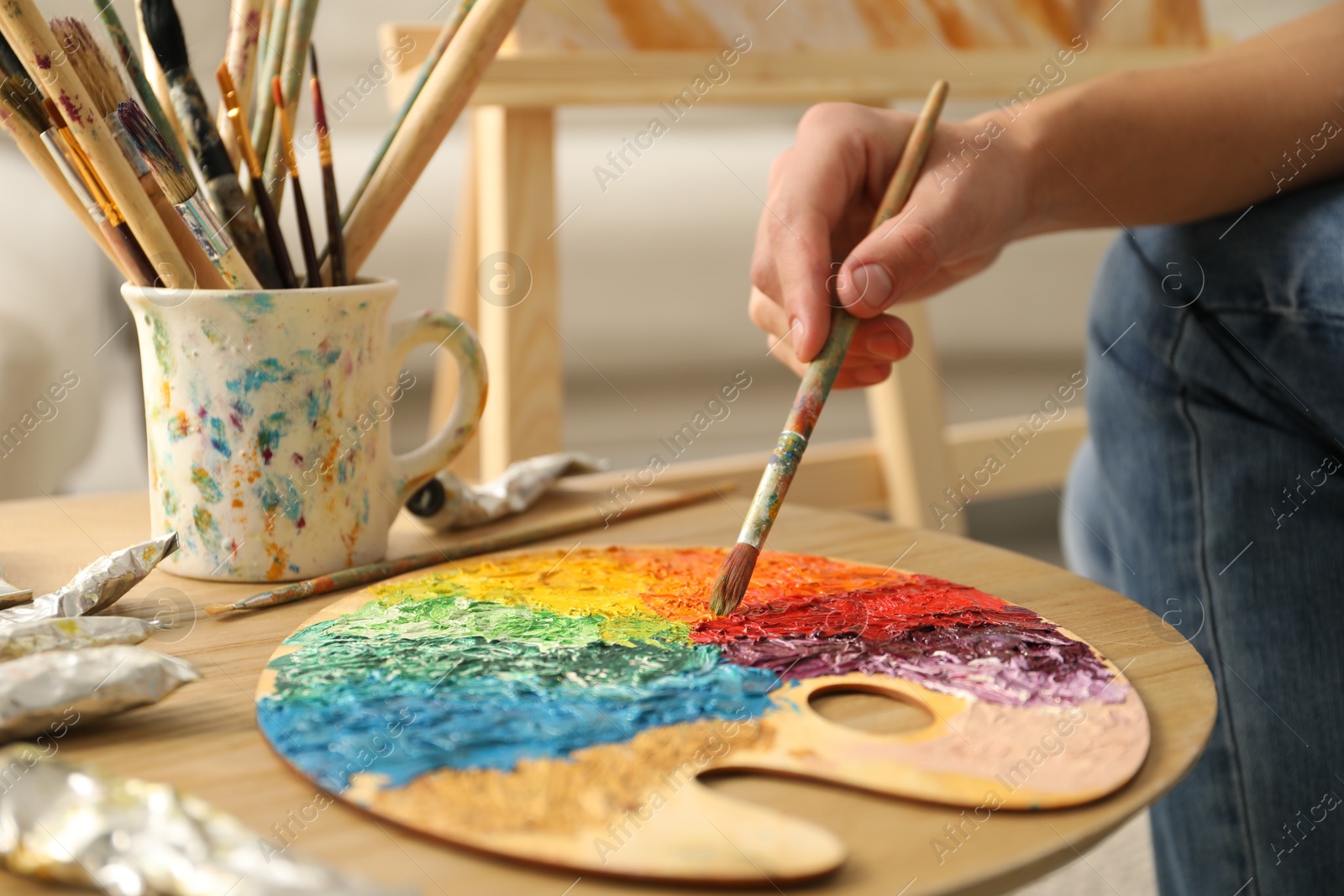 Photo of Man with paintbrush mixing paints on palette at wooden table indoors, closeup