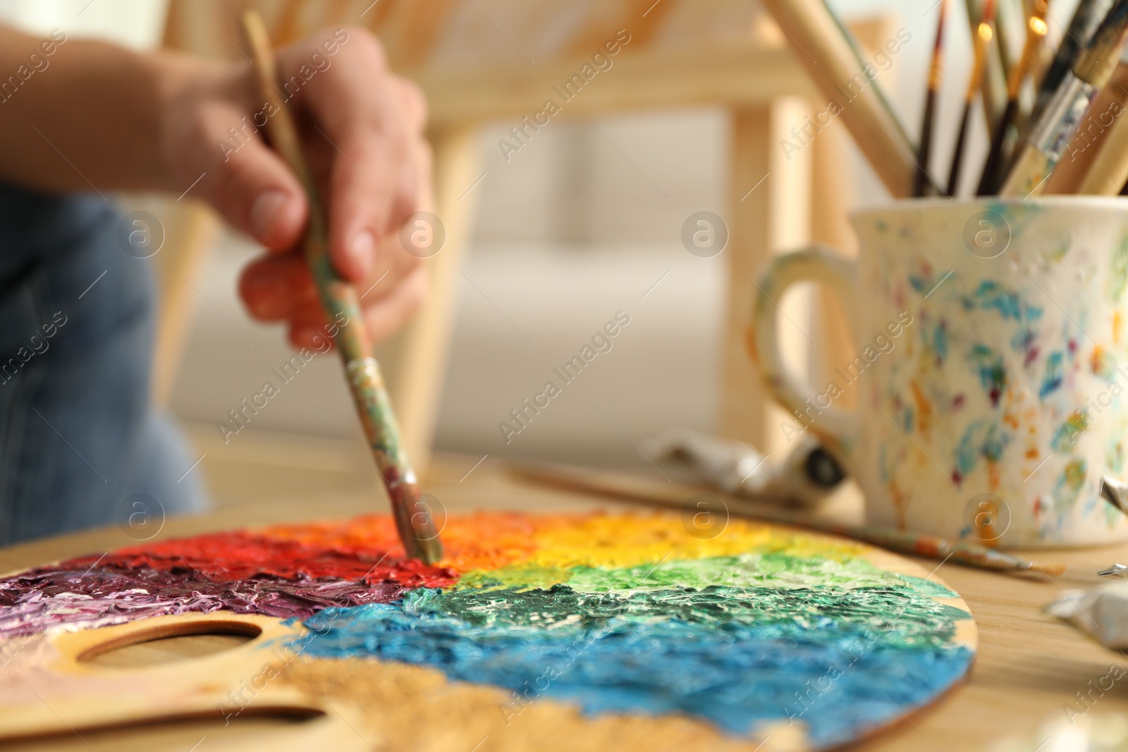 Photo of Man with paintbrush mixing paints on palette at table indoors, selective focus