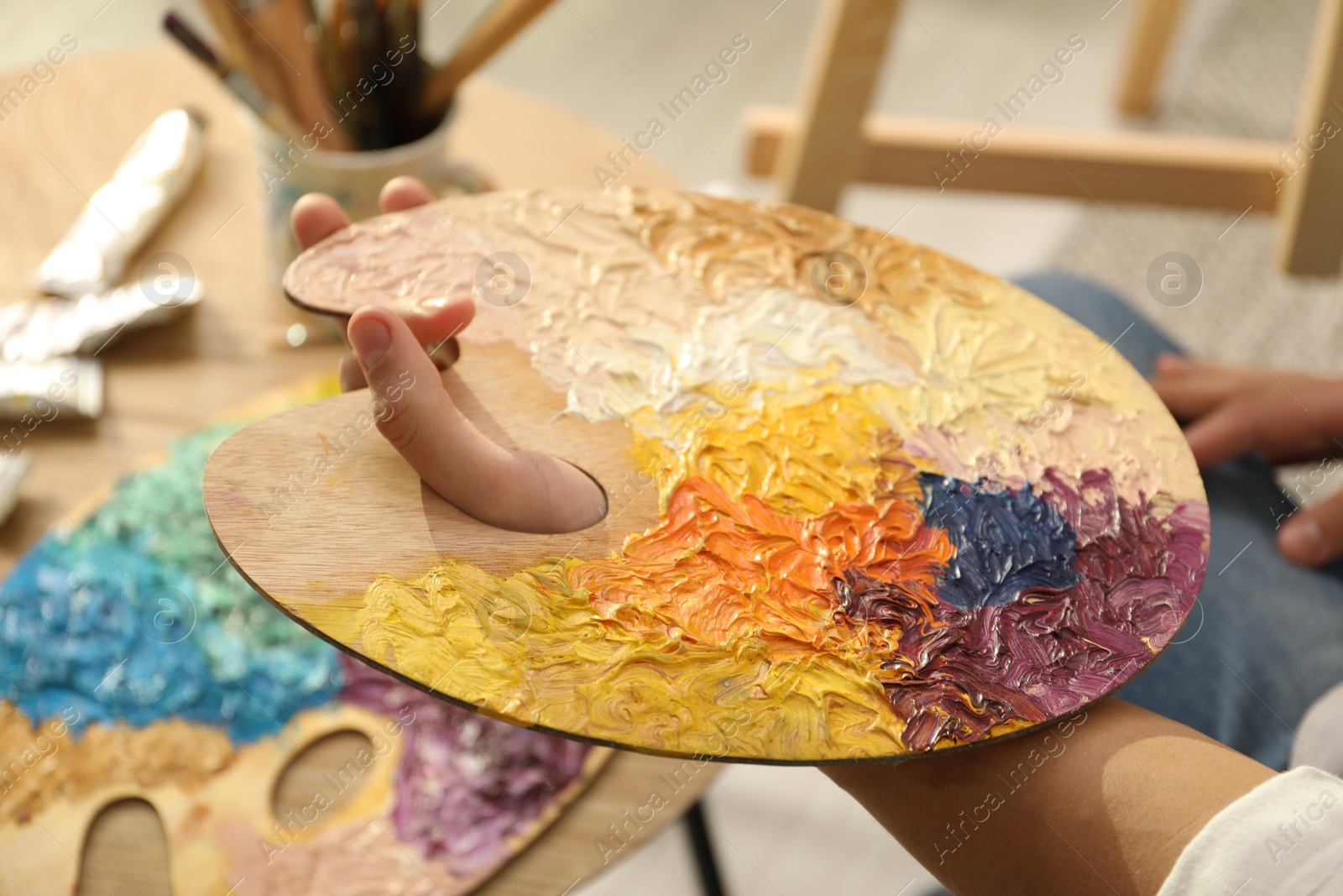 Photo of Man holding wooden palette with paints indoors, closeup