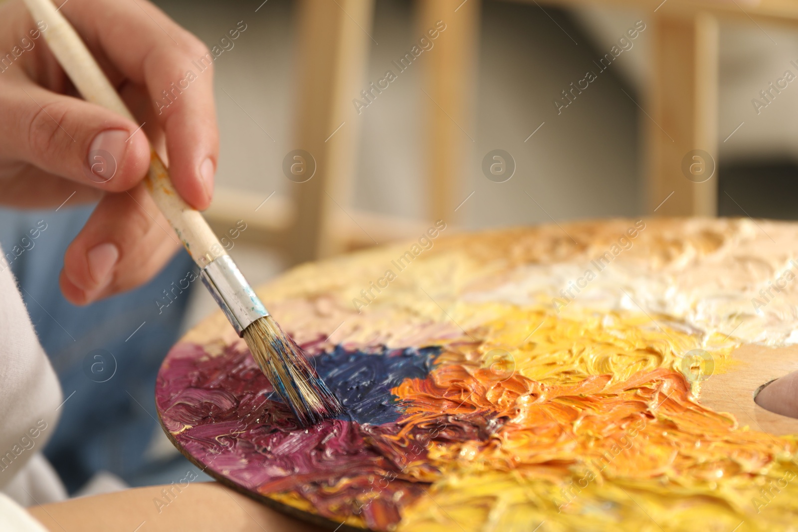 Photo of Man with paintbrush mixing paints on palette indoors, closeup