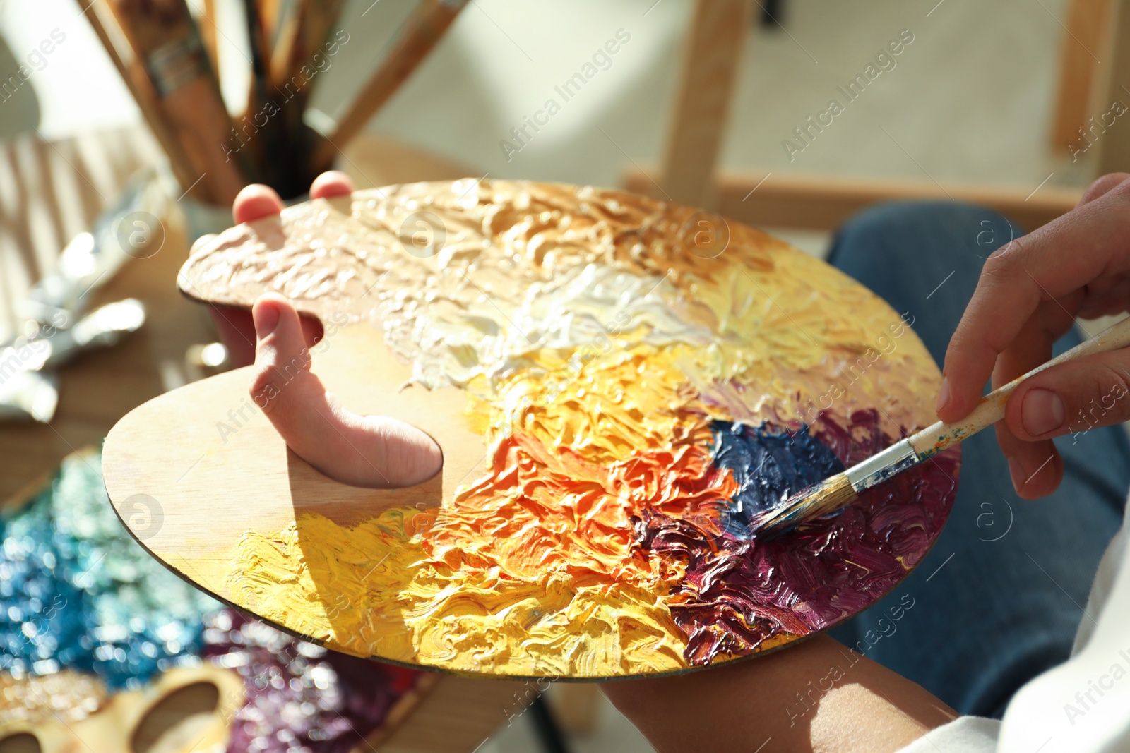 Photo of Man with paintbrush mixing paints on palette indoors, closeup