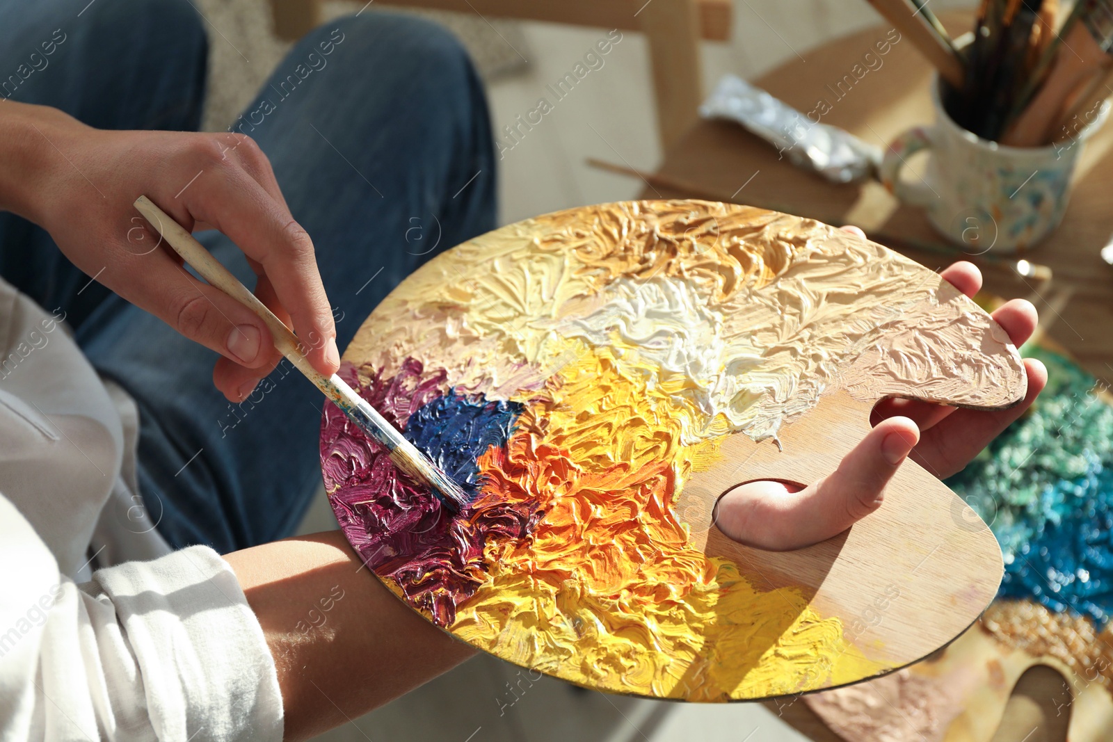 Photo of Man with paintbrush mixing paints on palette indoors, closeup