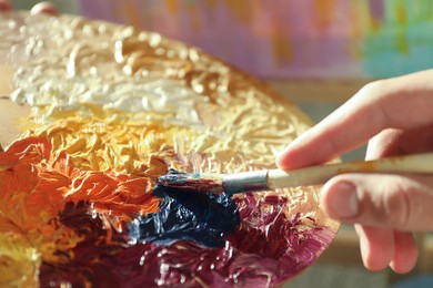 Photo of Man with paintbrush mixing paints on palette, closeup