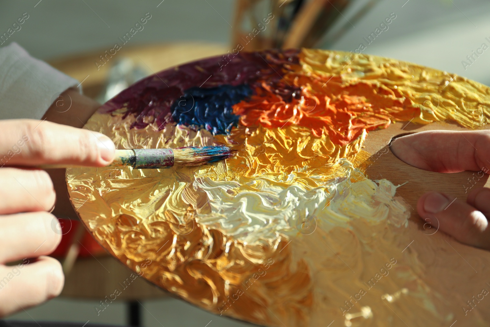 Photo of Man with paintbrush mixing paints on palette indoors, closeup