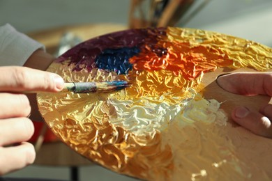 Man with paintbrush mixing paints on palette indoors, closeup