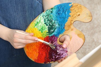 Woman with palette and paintbrush drawing picture, closeup