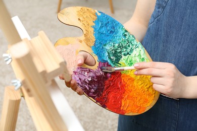 Woman with palette and paintbrush drawing picture, closeup