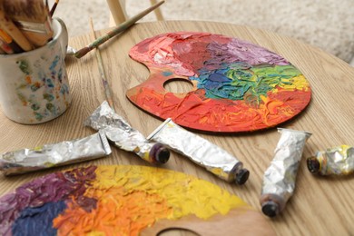 Photo of Palettes with bright paints, brushes and tubes on wooden table indoors, closeup