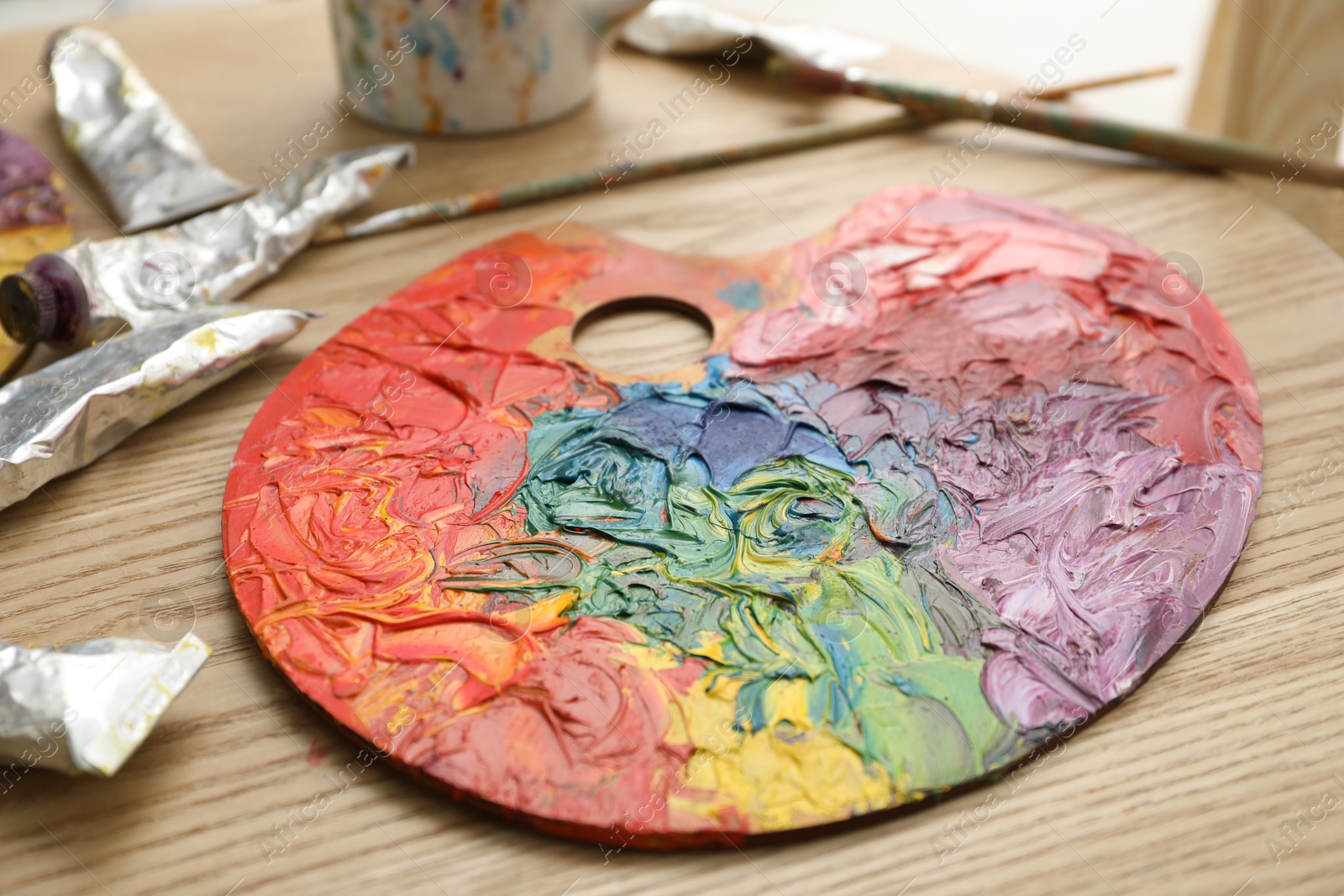 Photo of Palette with bright paints, brushes and tubes on wooden table, closeup