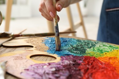 Woman with paintbrush mixing paints on palette at wooden table indoors, closeup