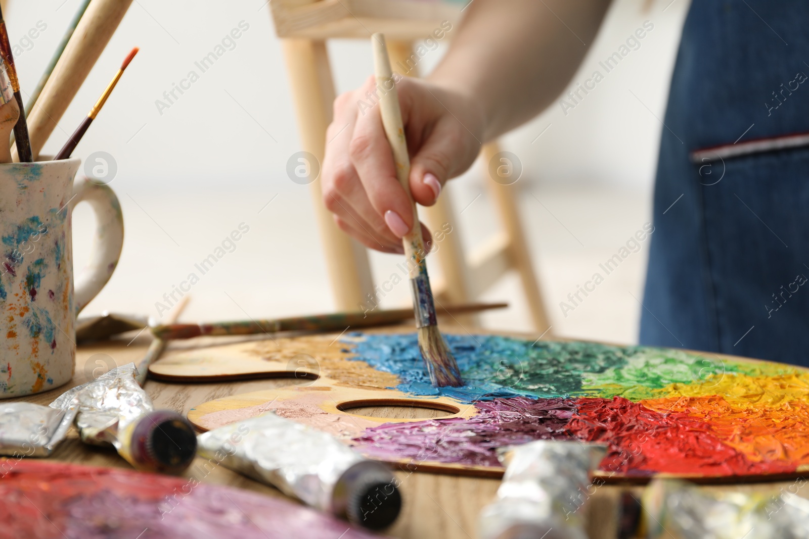 Photo of Woman with paintbrush mixing paints on palette at wooden table indoors, closeup