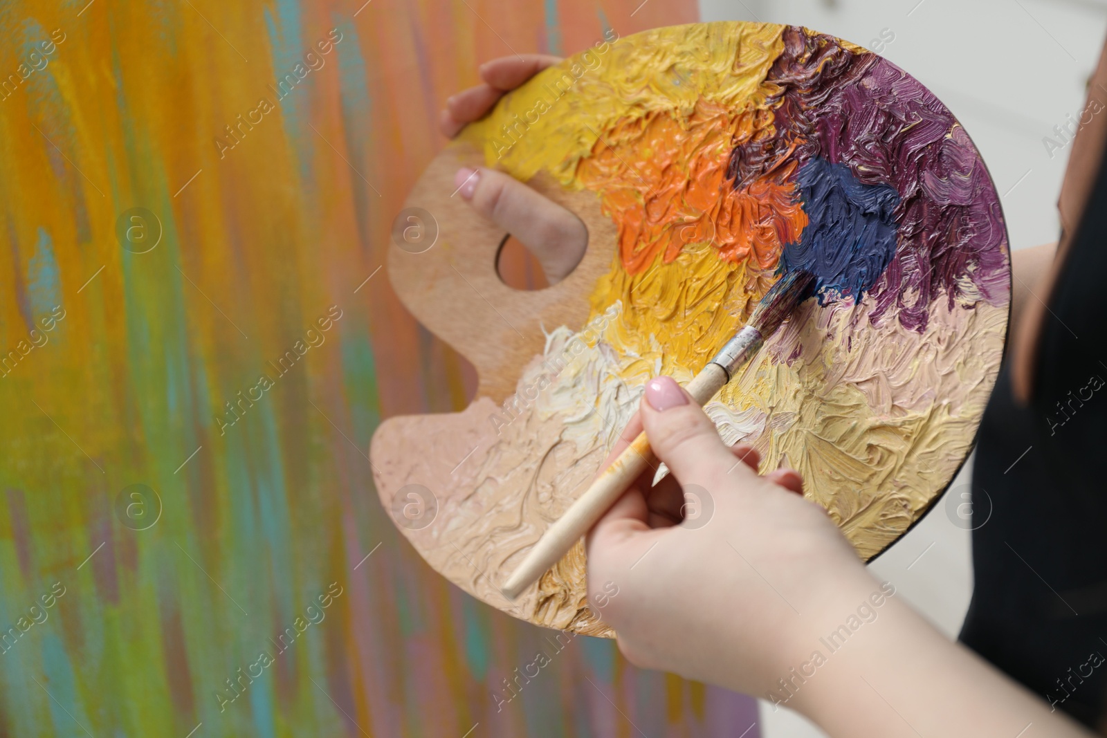 Photo of Woman with paintbrush mixing paints on palette near picture, closeup