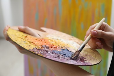 Photo of Woman with paintbrush mixing paints on palette near picture, closeup