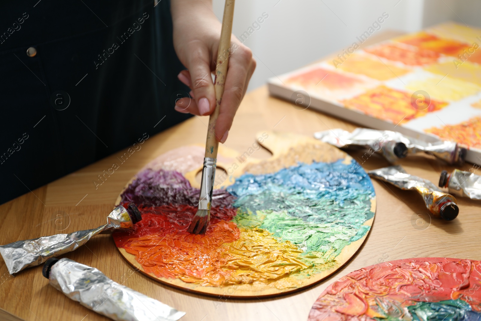 Photo of Woman with paintbrush mixing paints on palette at wooden table, closeup