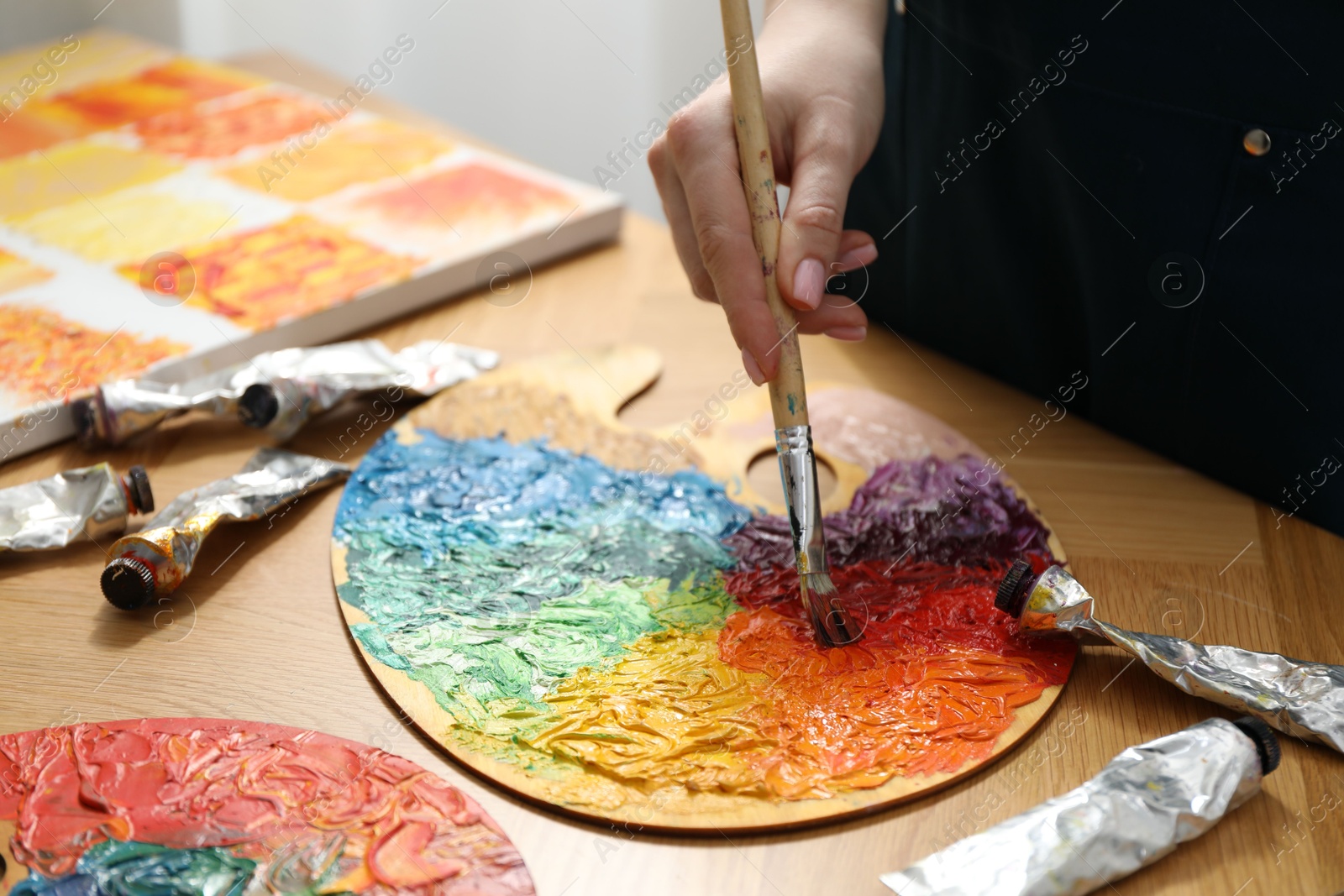 Photo of Woman with paintbrush mixing paints on palette at wooden table, closeup