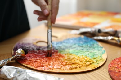 Woman with paintbrush mixing paints on palette at wooden table, closeup