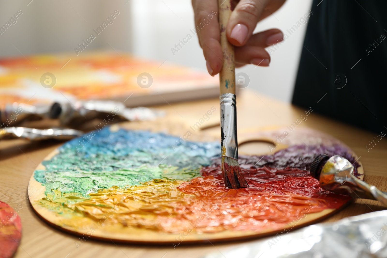 Photo of Woman with paintbrush mixing paints on palette at wooden table, closeup